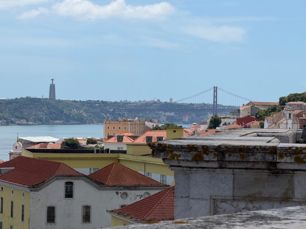 Ausblick über Lissabon mit bunten Häuserdächern, der Jesus-Statur und einer Brücke.